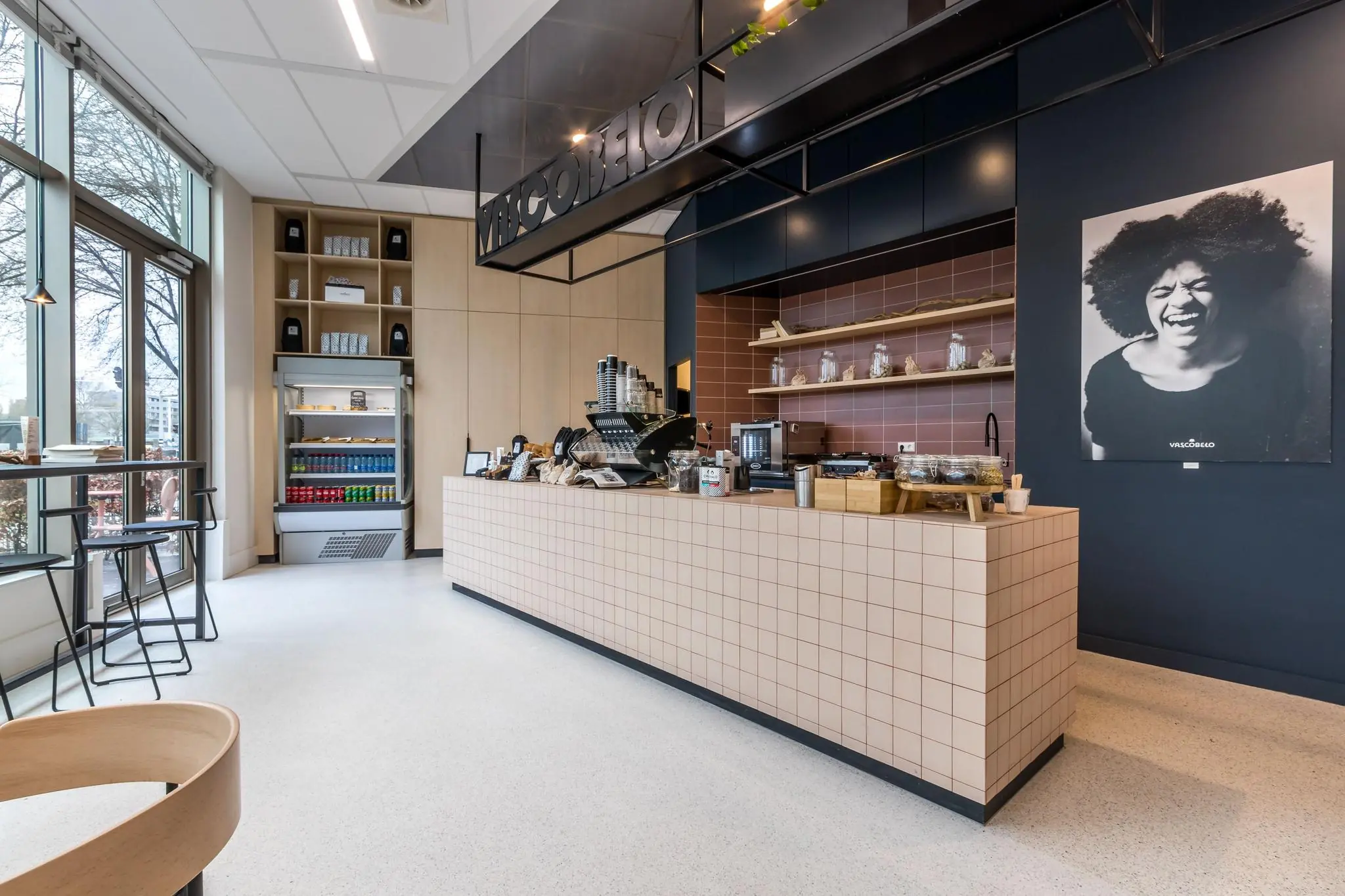 Moderne koffiebar aan de Vliegend Hertlaan met strakke inrichting, grote ramen en een opvallend portret aan de muur.